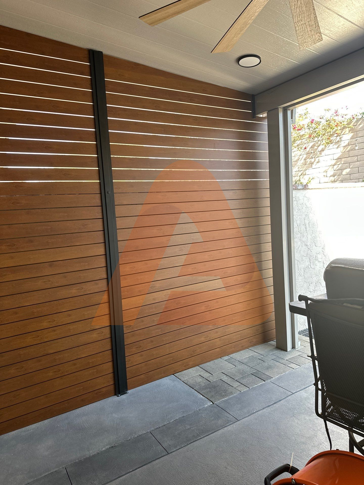 Woodgrain horizontal aluminum slat privacy screen with dark aluminum posts beside a covered patio