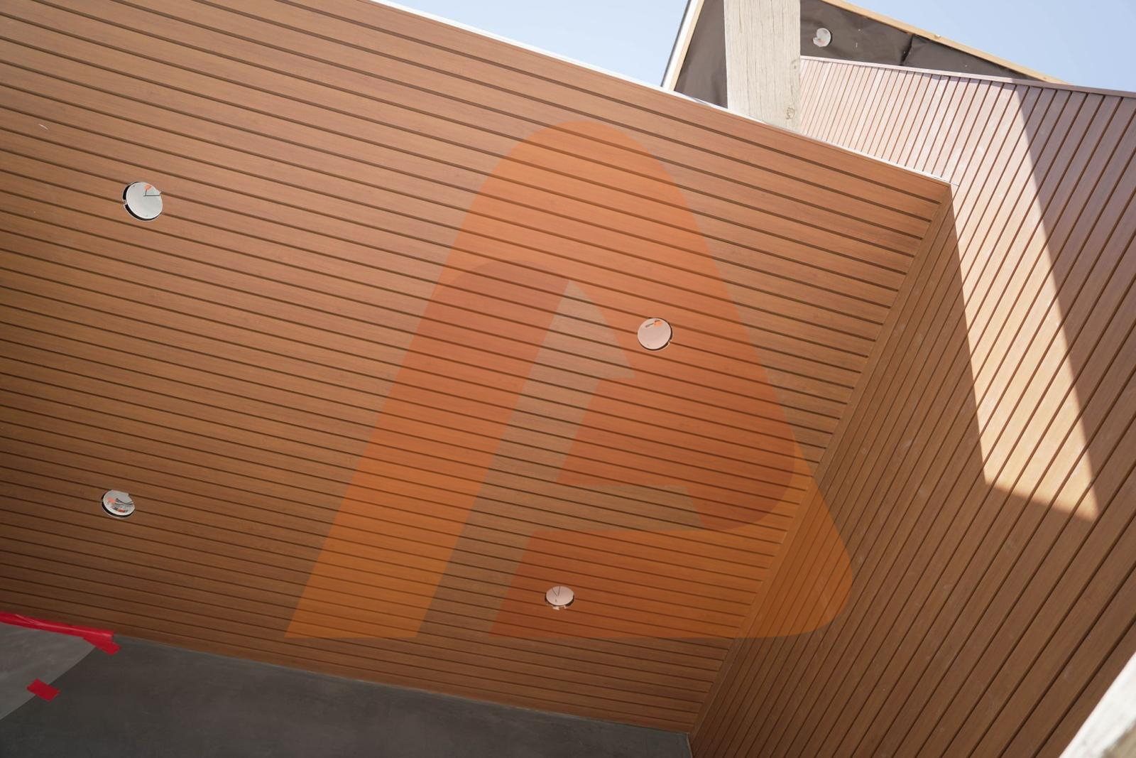 Real installed wood-look aluminum cladding wrapping an exterior soffit and wall with recessed lights