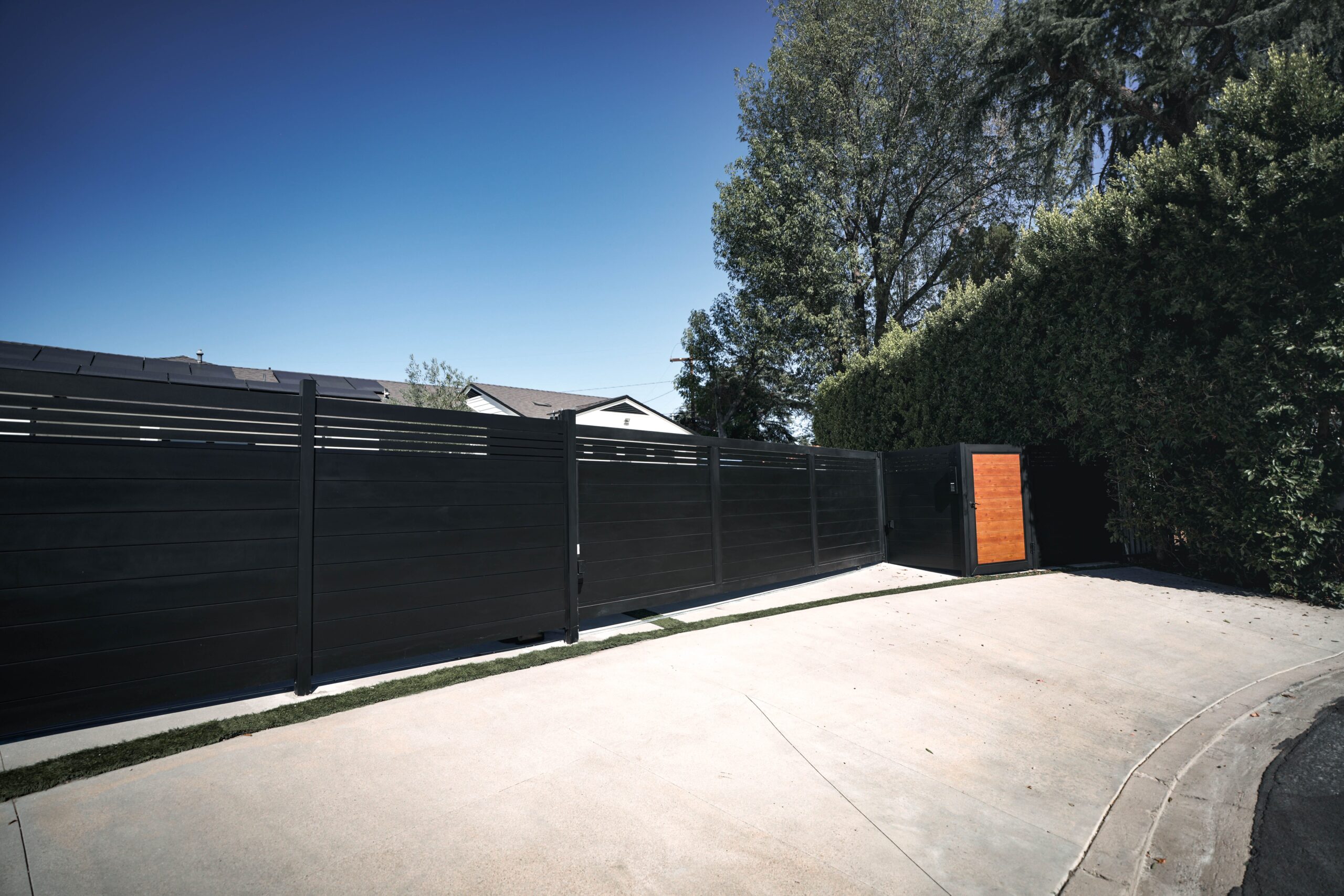 Large modern black aluminum sliding driveway gate with a framed wood-look pedestrian gate