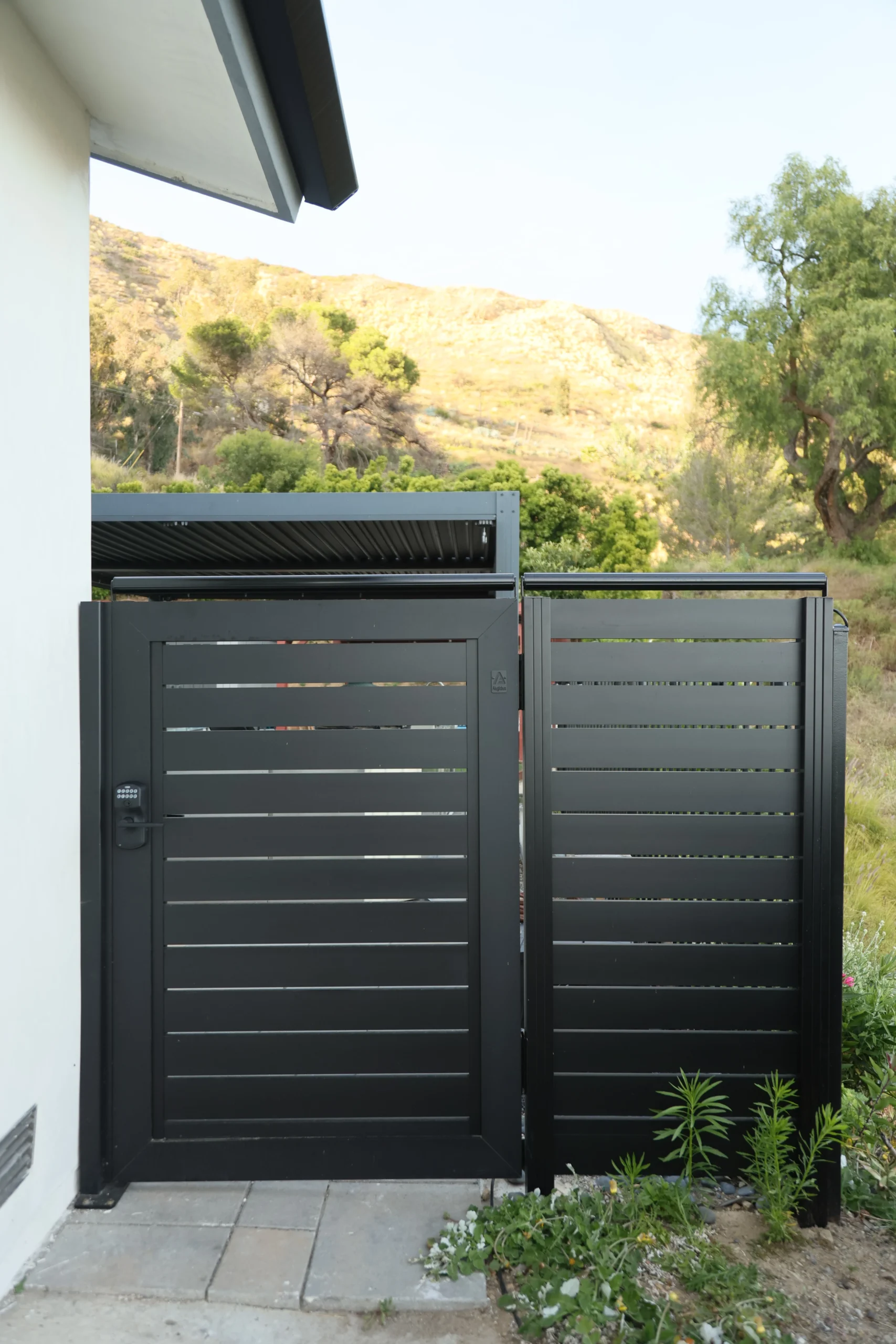 Tall black aluminum gate with coyote roller and hillside view