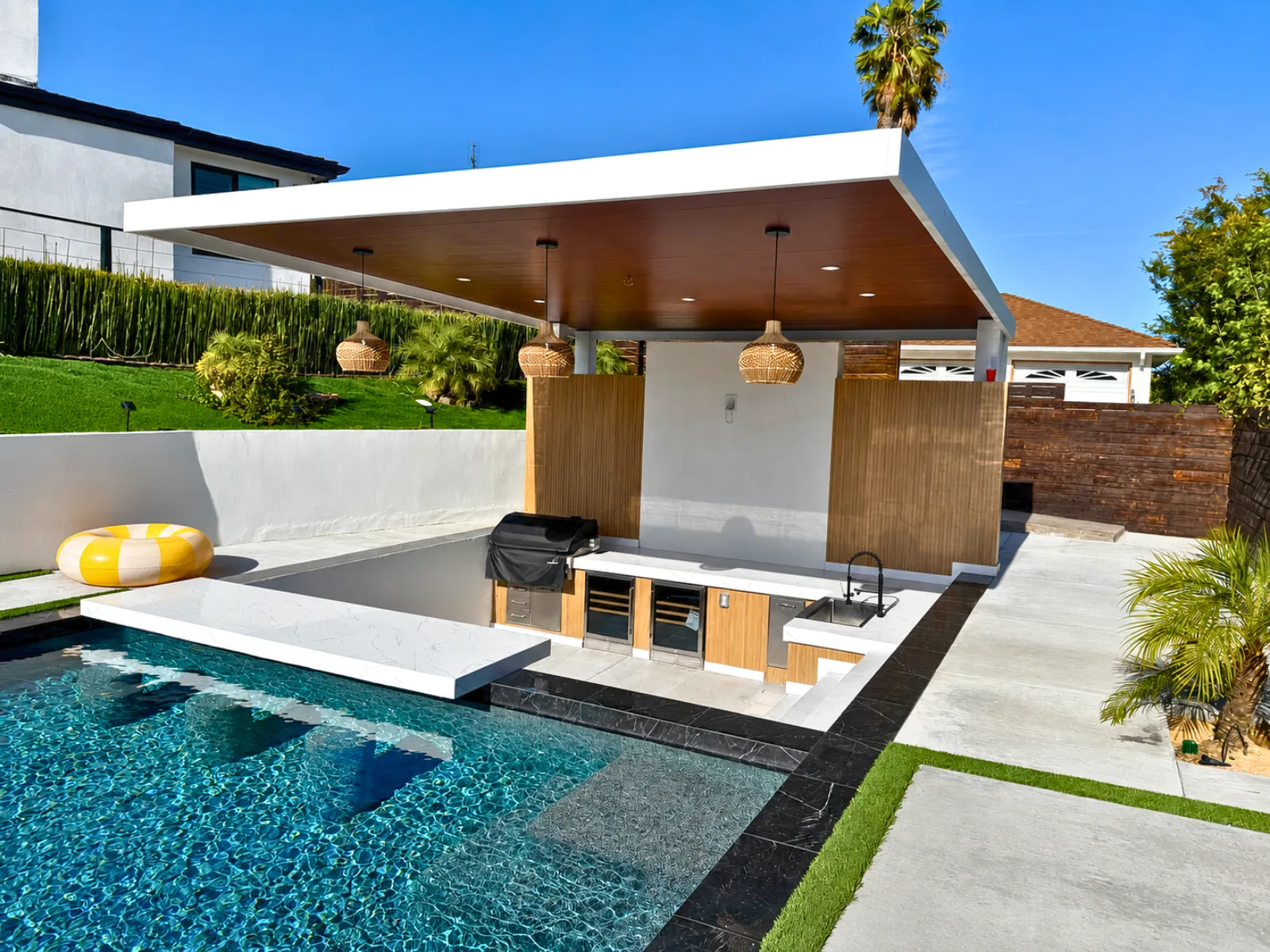 Modern poolside insulated aluminum patio cover with a white frame, wood-look ceiling, and pendant lights
